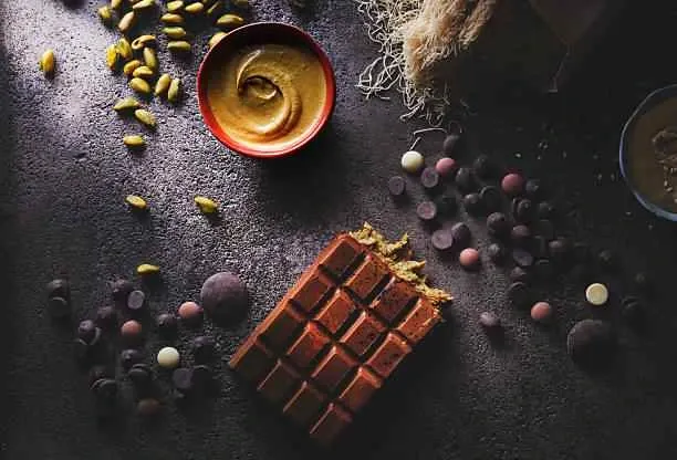 Dubai chocolate bar ingredients flat lay – milk chocolate bar with pistachio cream, chocolate chips and pistachios on dark background